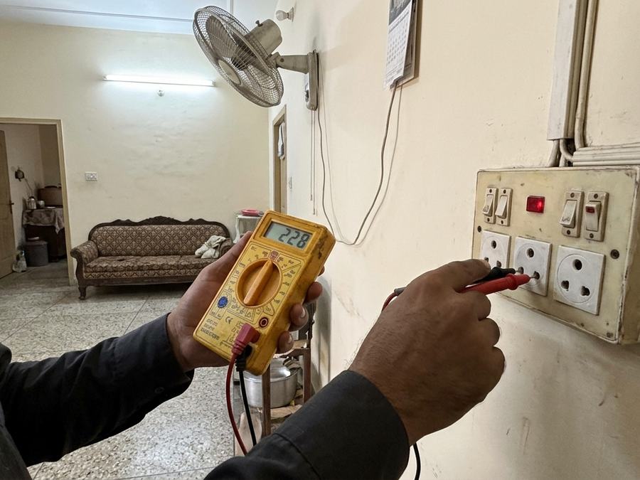 Electrician testing a wall socket with a multimeter in a living room